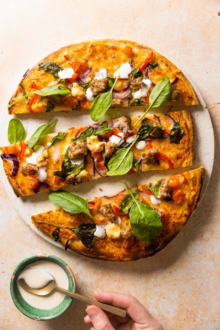 Salsicciapizza med ajvarsaus, paprika og spinat, servert med hvitløksdressing